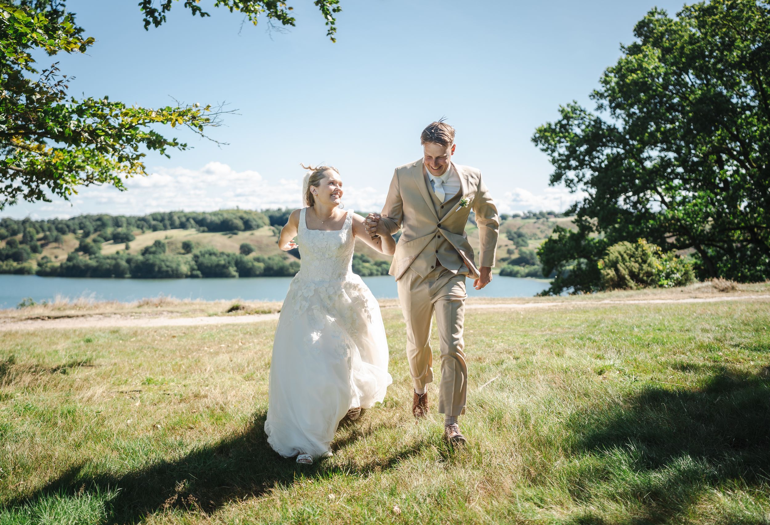 A couple shares a romantic moment in a sun-drenched meadow with rolling hills and trees in the background.