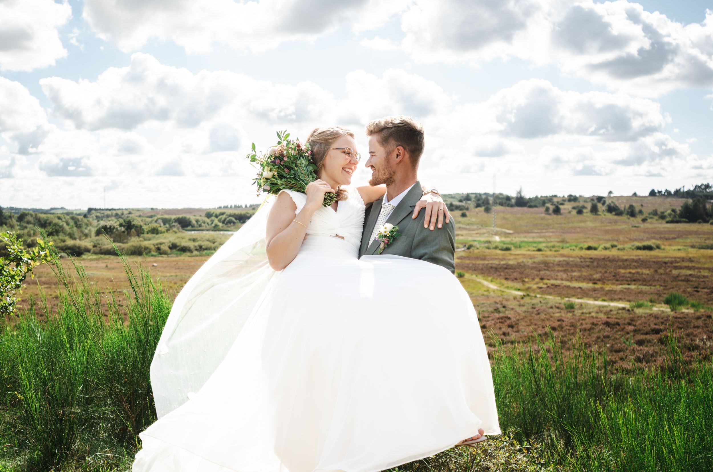 Bride and groom share romantic moments in scenic mountain meadow with flowing white wedding dress and natural backdrop.