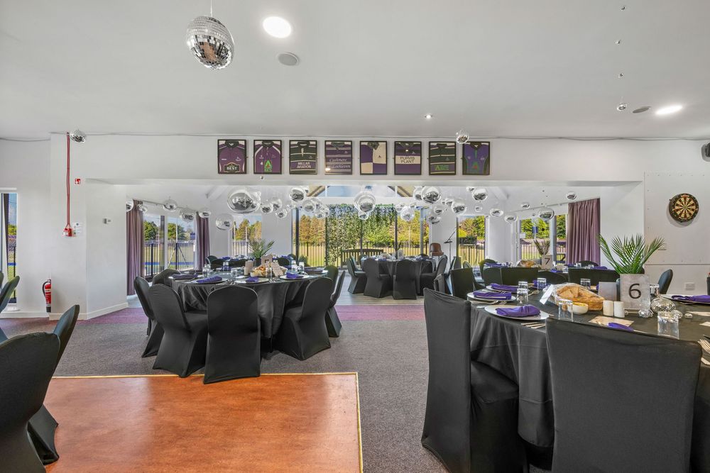 Modern event venue with black tablecloths and chairs under disco balls and natural lighting.