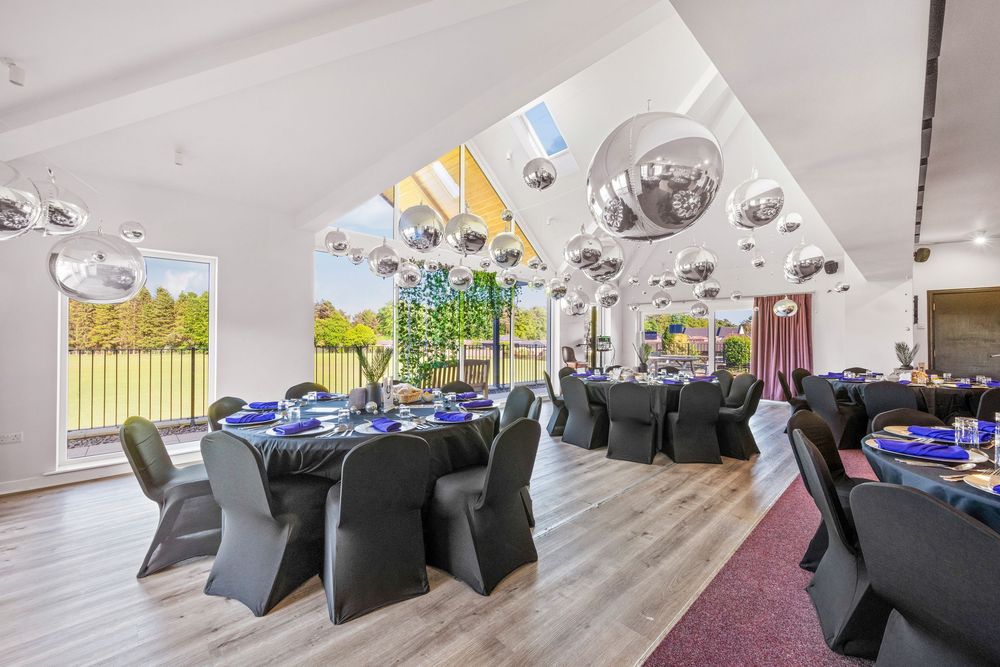 Elegant banquet hall with vaulted ceiling, black chairs and tables, and large windows overlooking greenery.