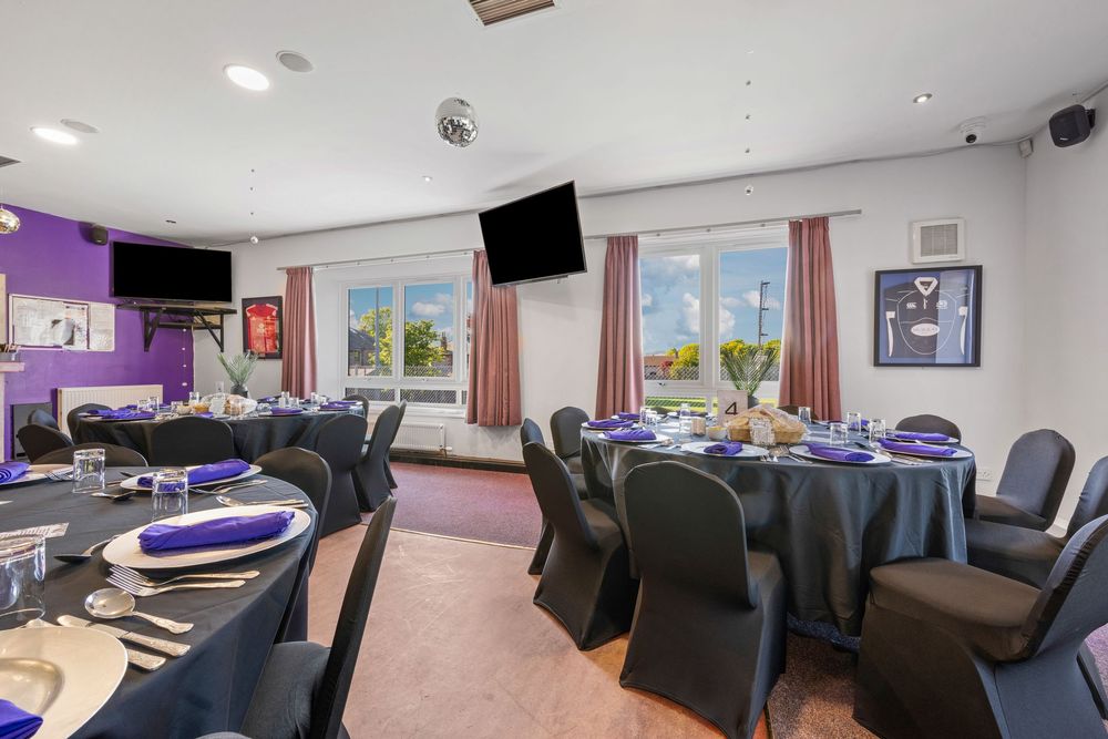Purple-accented dining room with round tables, black chair covers and panoramic windows.