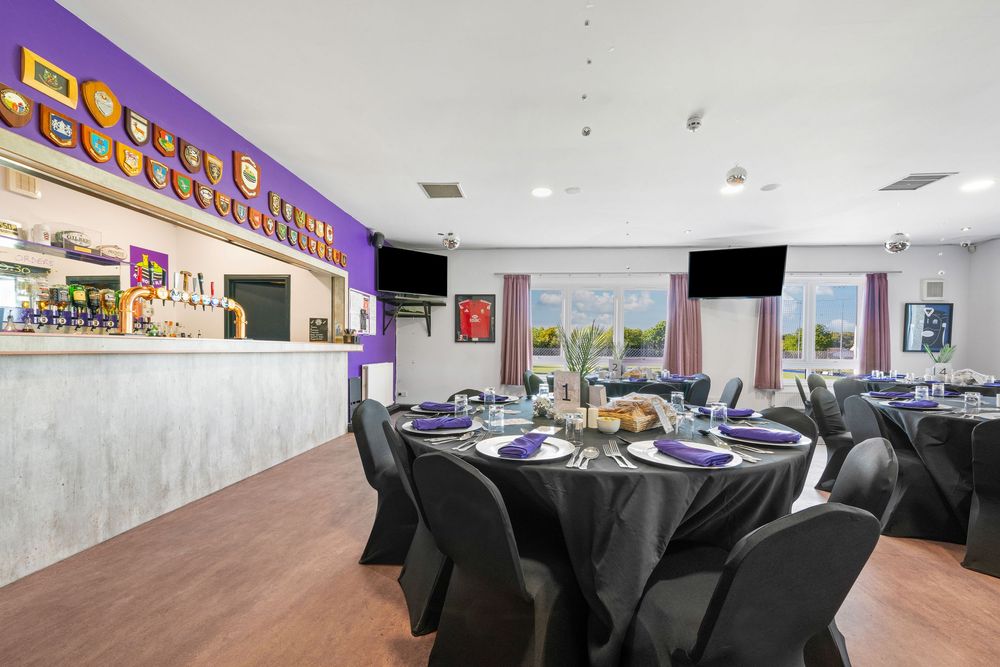Modern restaurant interior with purple walls, black furniture and bar area.