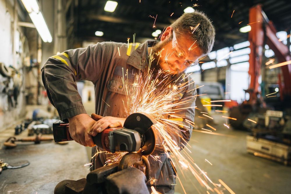 Industrial worker using angle grinder with bright orange sparks flying in metalworking shop.