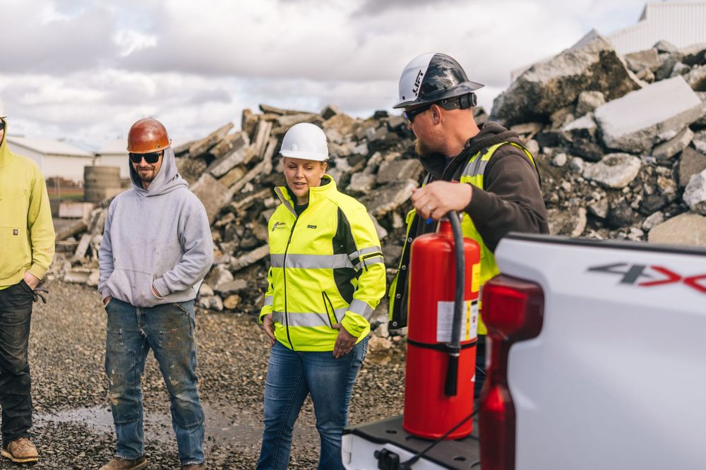 Construction workers in safety gear inspect and discuss project details at an outdoor worksite.