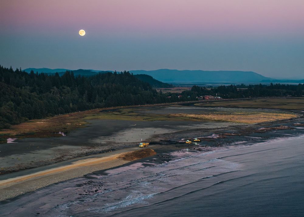Panoramic aerial view of a coastal landscape with mountains and beaches at dusk with a full moon rising.
