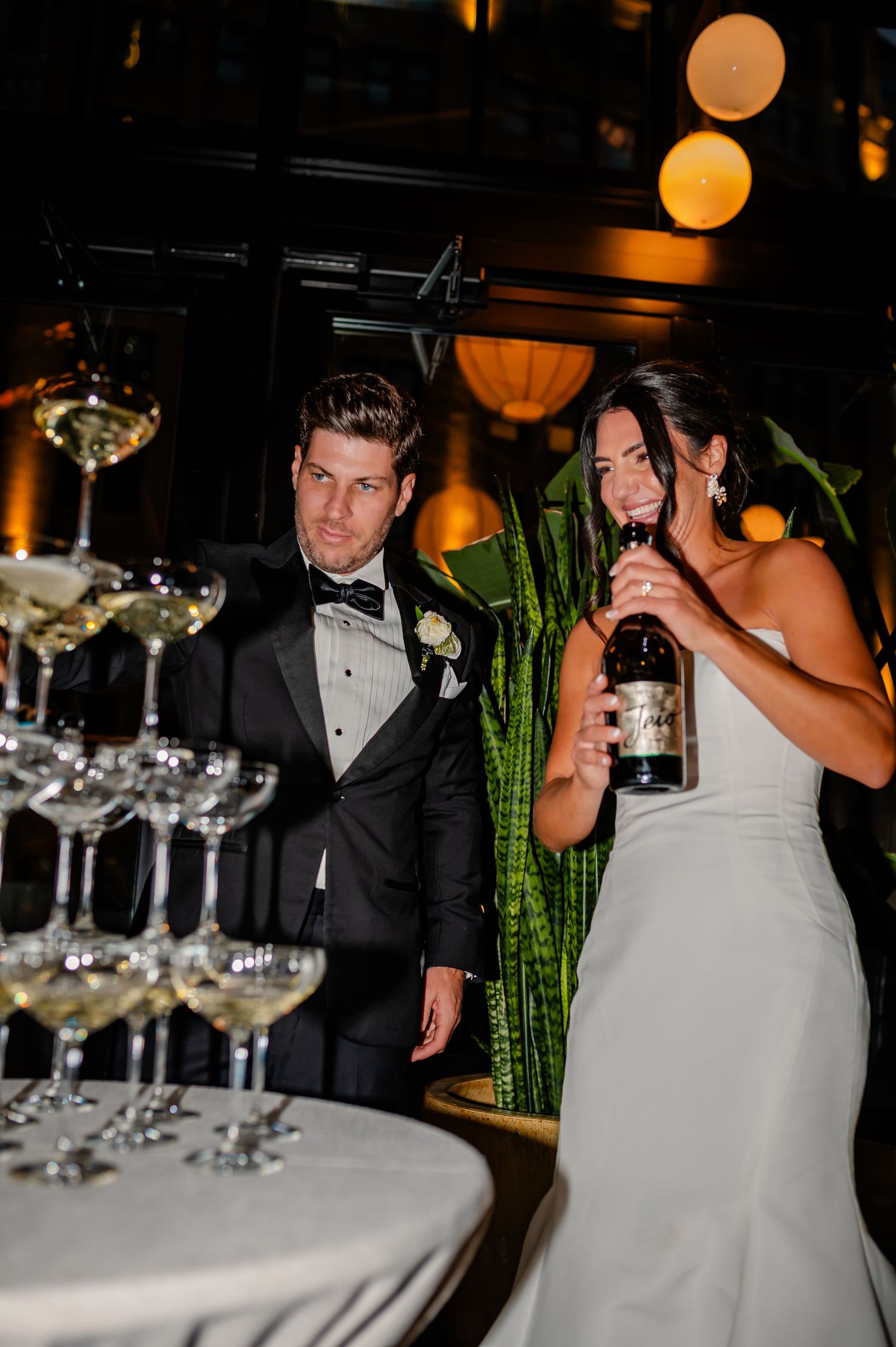A couple in formal wedding attire dancing near a pyramid of champagne glasses at an elegant reception.