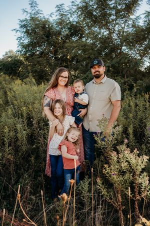 A family stands together in a natural outdoor setting with tall grass and trees during golden hour.