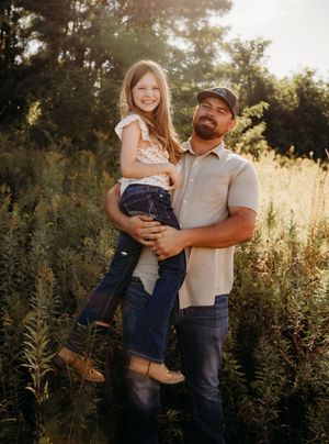 A pair share tender moments in a sunlit field of tall grass and wildflowers during a golden hour photoshoot.