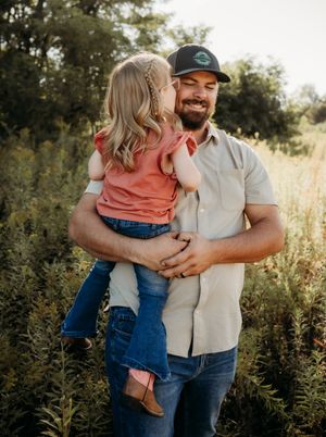 A couple embraces and laughs together in a natural outdoor setting with golden sunlight filtering through trees.