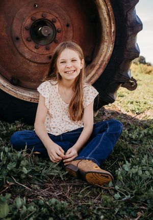 A sequence of candid portraits taken near a rustic tractor wheel in a grassy outdoor setting.