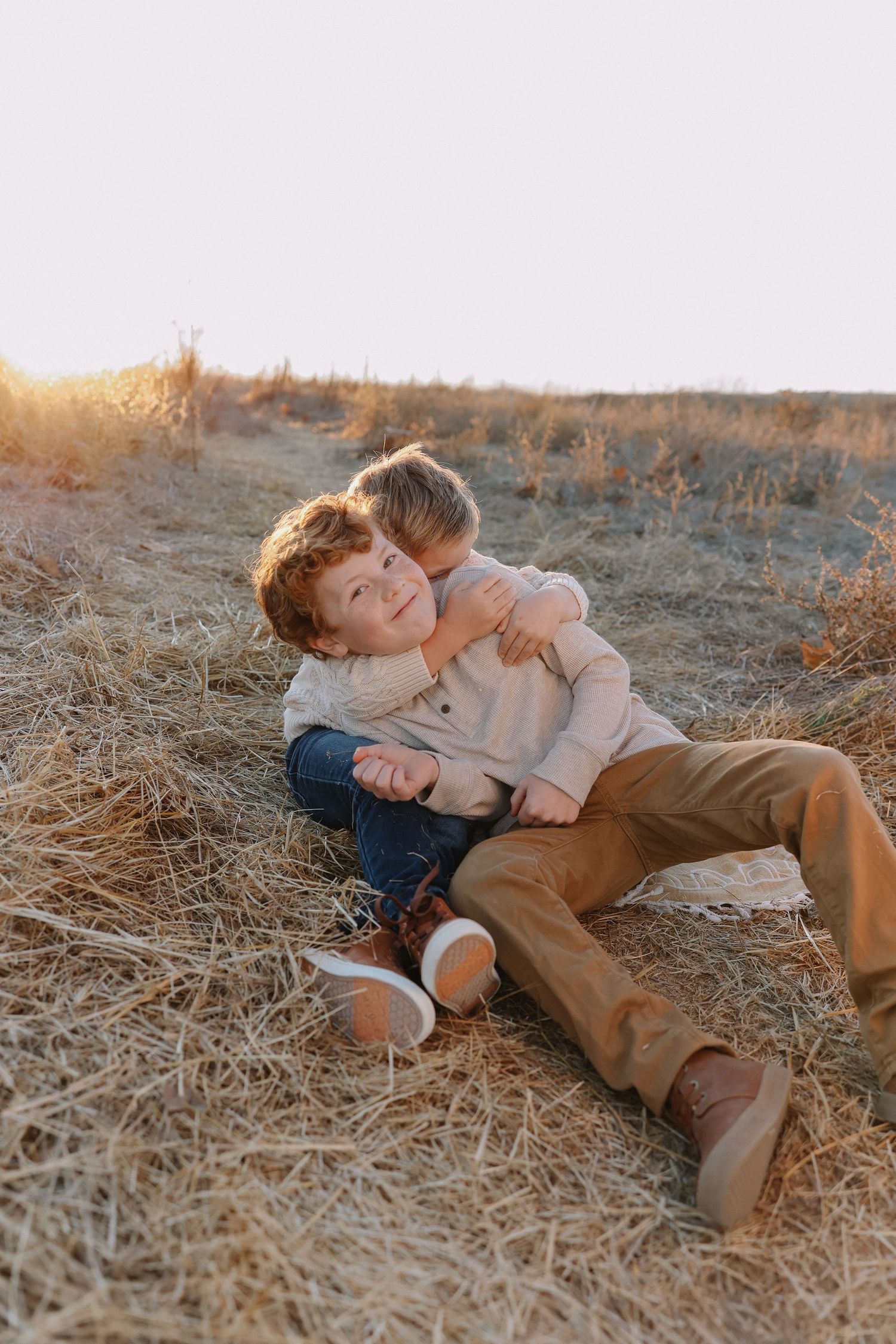 Two children play and laugh together while lying in a golden field at sunset for their family photos