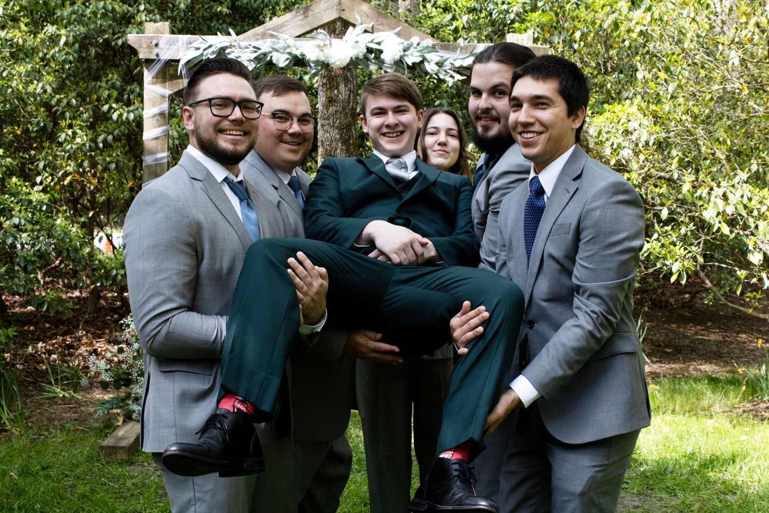Groomsmen in grey suits laughing and posing together outdoors.