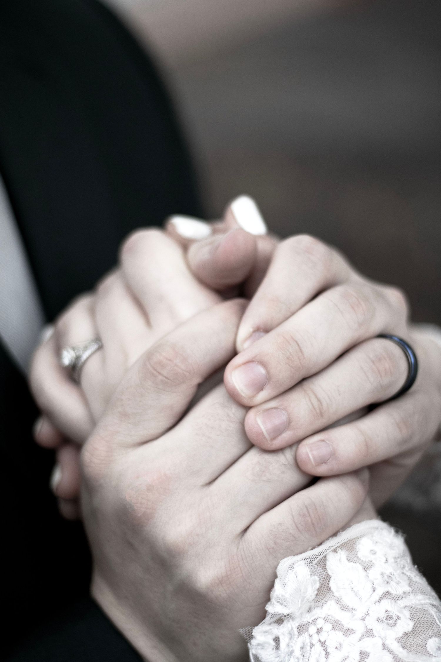 Close-up of clasped hands with delicate lace sleeve detail in black and white.