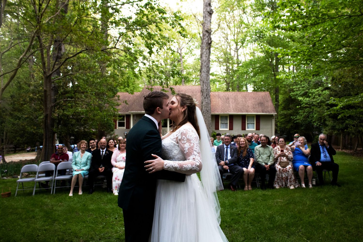 Wedding celebration in a wooded outdoor setting with guests watching the ceremony.