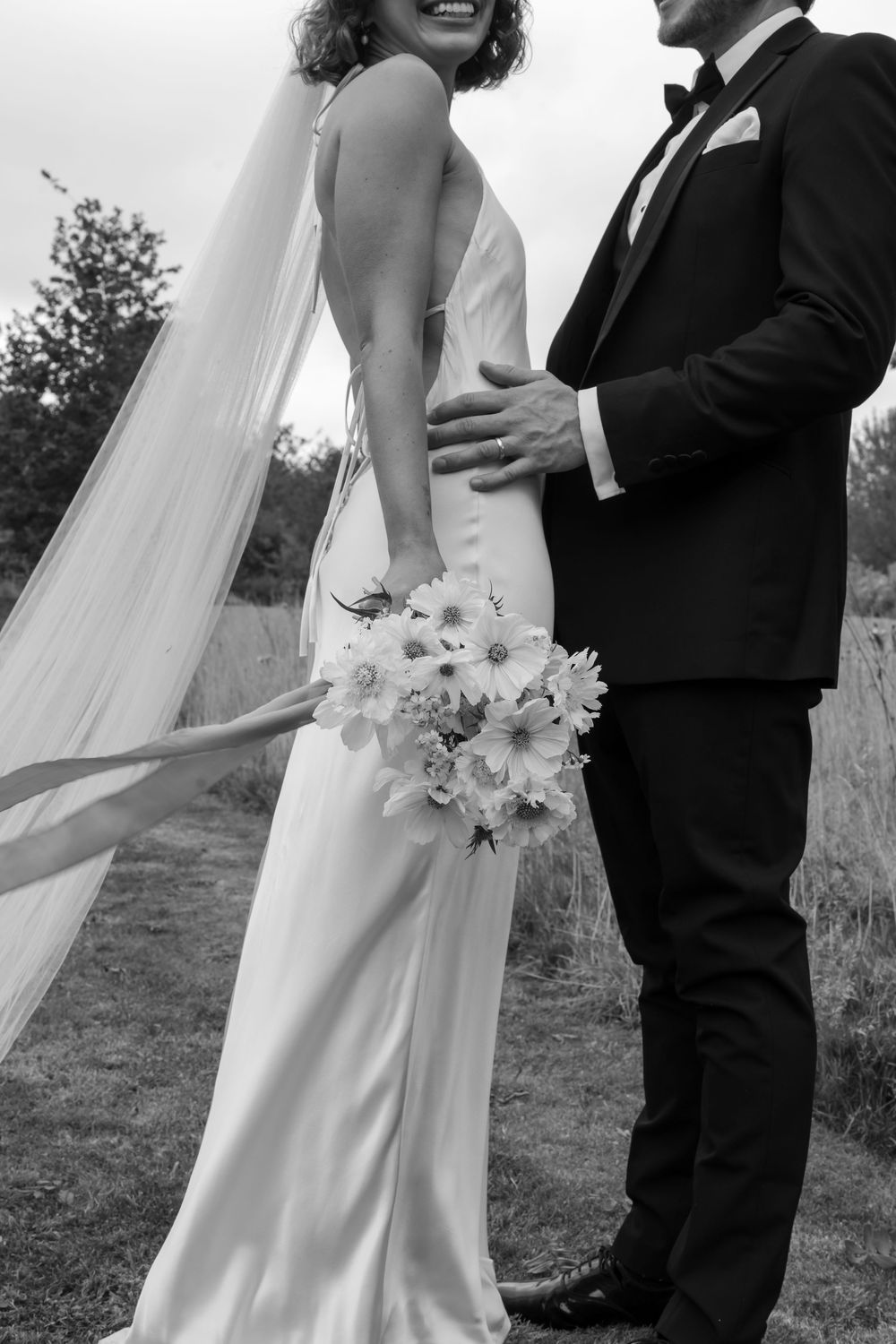 A romantic black and white wedding photo showing a couple embracing outdoors, with the bride holding a delicate floral bouquet.
