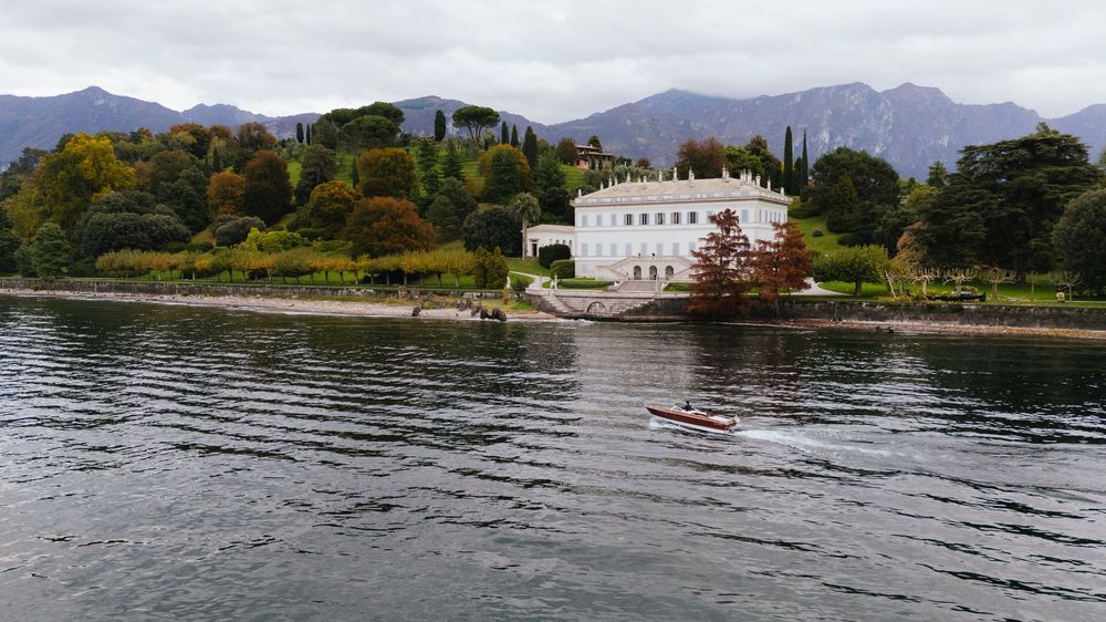 Panoramic view of coastal homes and buildings along a serene waterfront with boats and lush greenery.