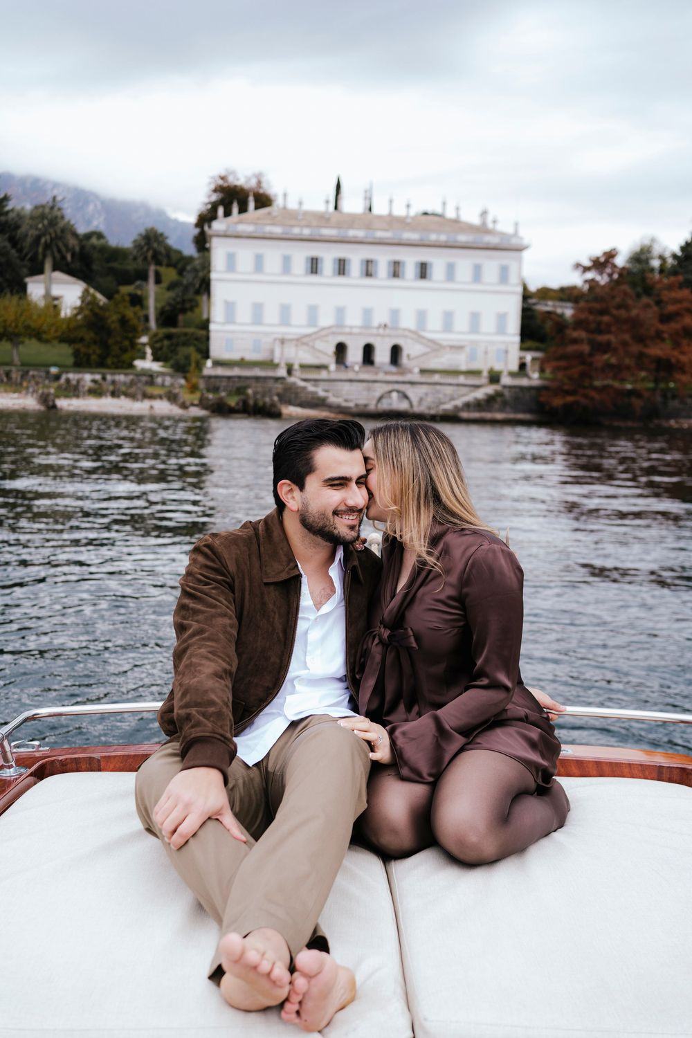 Romantic couple enjoying an intimate boat ride along a waterfront with elegant white buildings in the background.