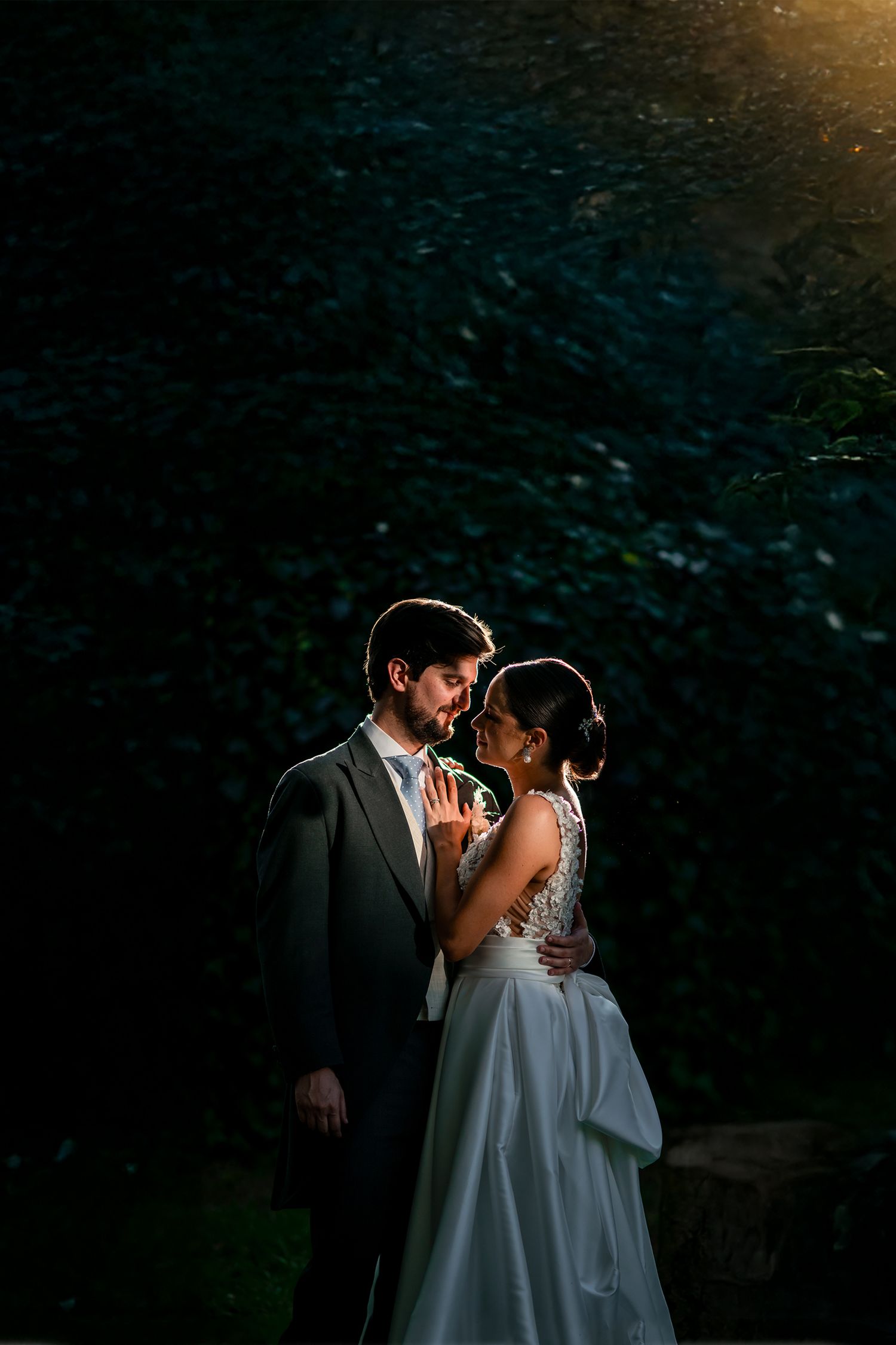 Romantic sunset wedding portrait with couple embracing in dramatic backlit evening light.