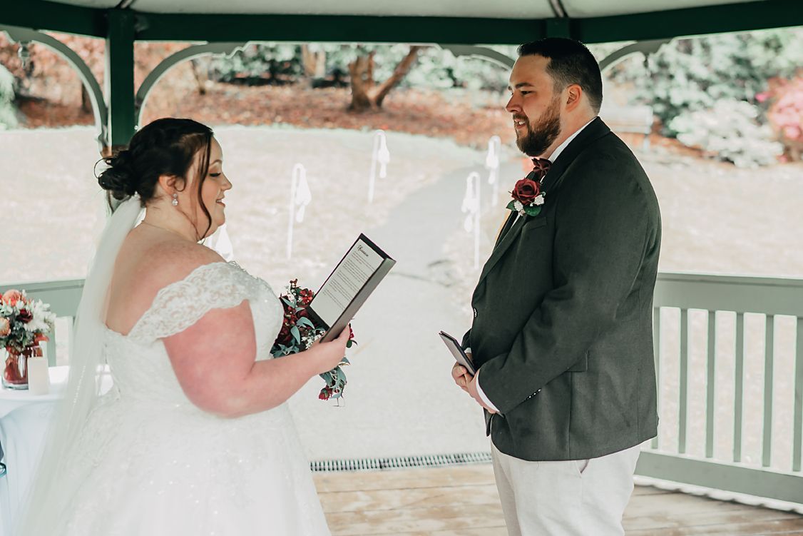 A bride and groom exchange vows under a white gazebo during an outdoor wedding ceremony.