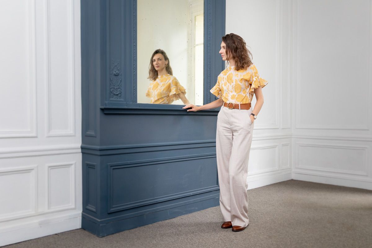 Two people wearing retro-inspired outfits interact at a blue reception desk in an elegant white-walled room.