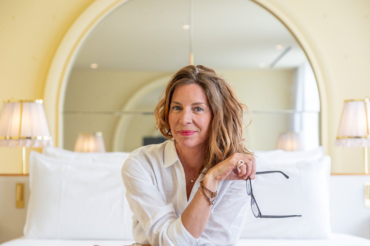 Woman relaxing in plush white bedding at luxury hotel room with bright natural lighting.