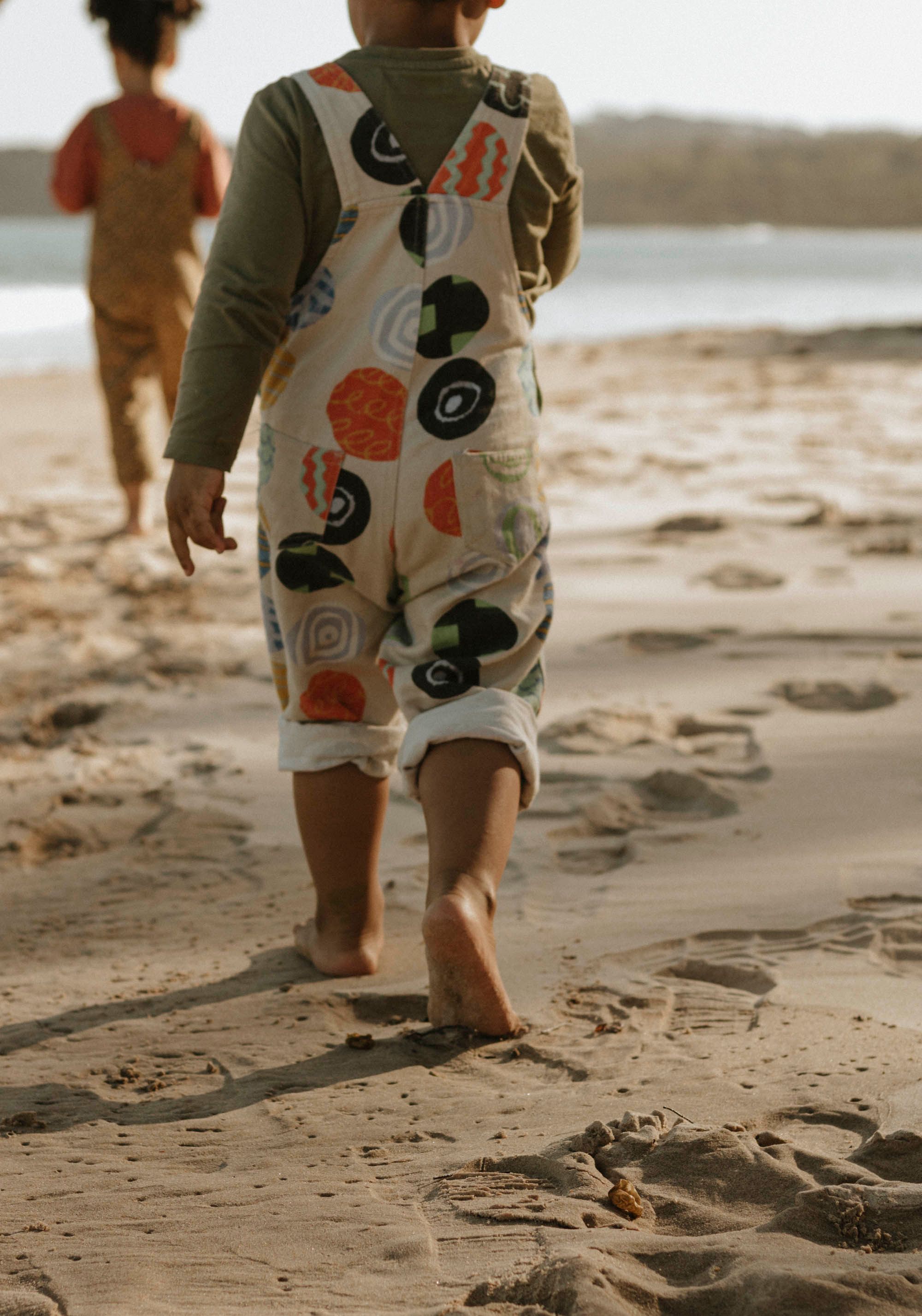 Small feet walking in the sand wearing patterned clothing on a beach.