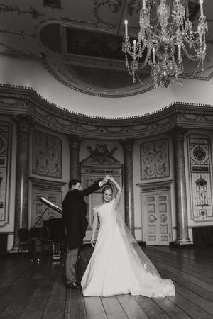 A black and white wedding photograph series showing a couple dancing in an elegant ballroom with ornate chandeliers and decor.