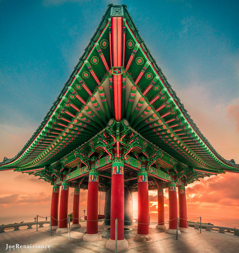 Traditional Korean pagoda pavilion with red pillars and ornate green roof against a vibrant sunset sky.