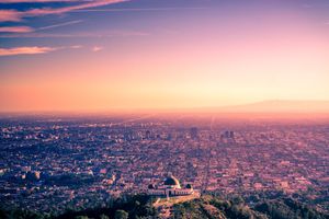 Skyline of Los Angeles with urban sprawl stretching to horizon under vibrant pink sunset clouds.