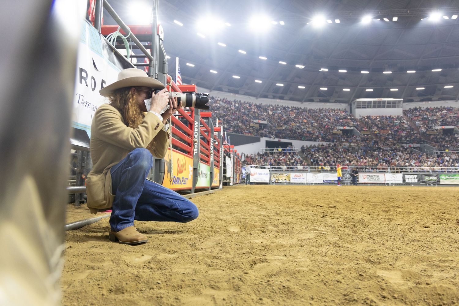 A row of riders competing in a rodeo arena under bright stadium lights with sandy ground visible.