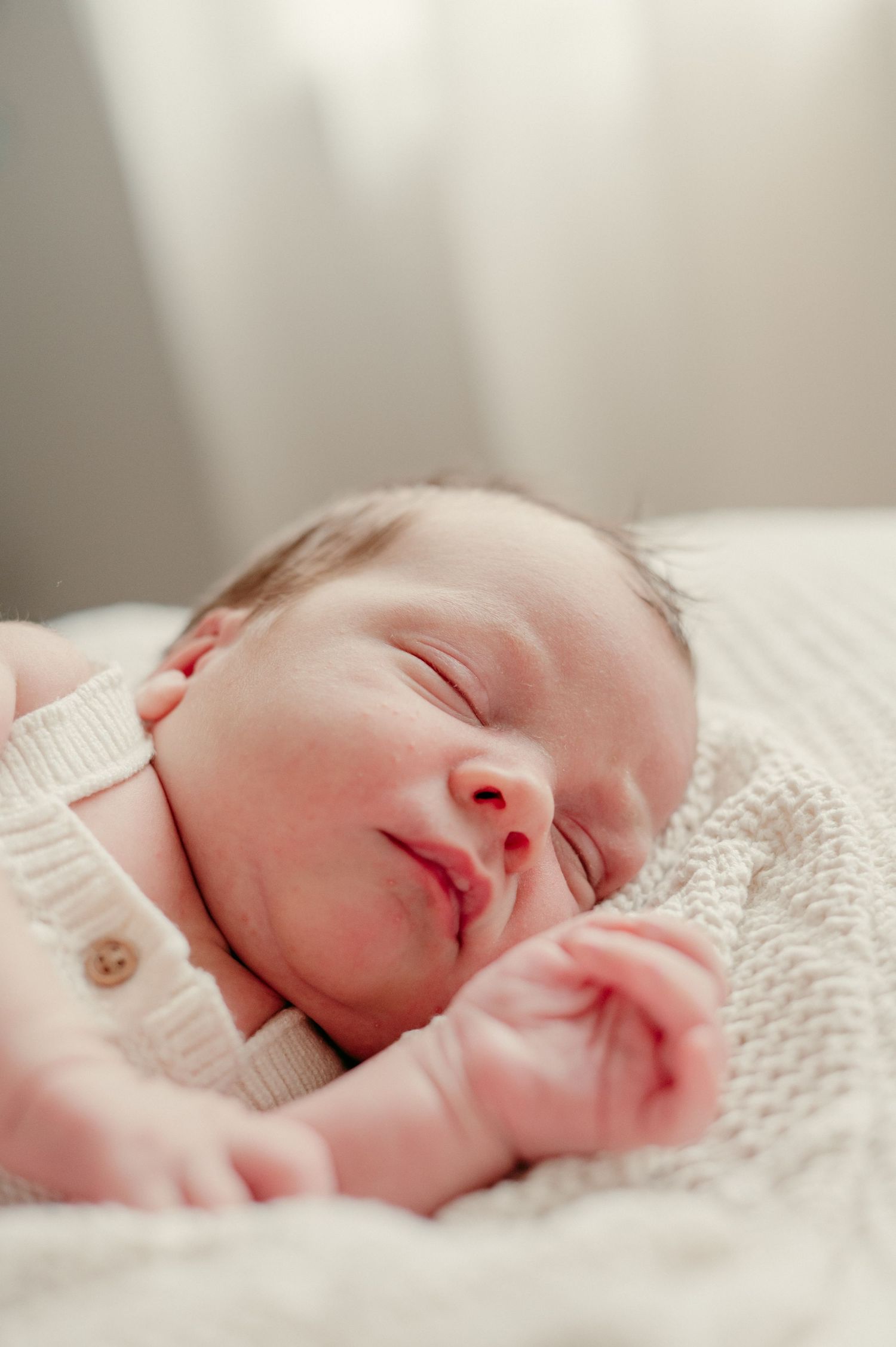 Peaceful sleeping newborn baby in white clothing on soft bedding.