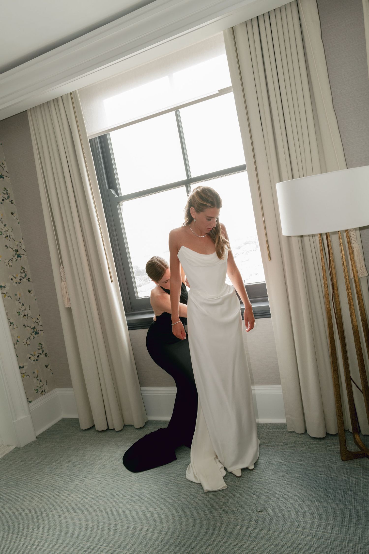 Final wedding dress fitting shows a seamstress making last-minute adjustments in an elegant room with natural light.