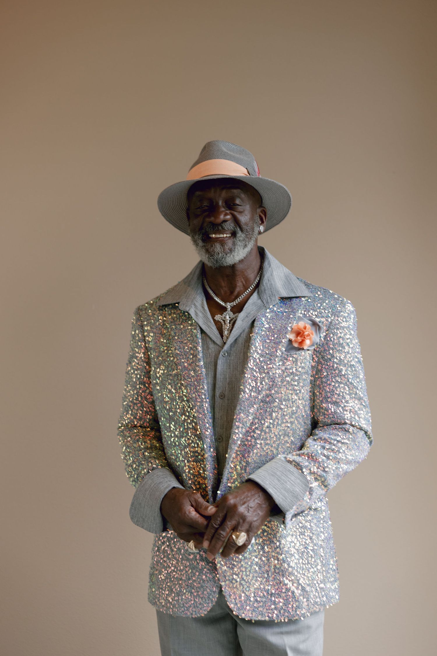 Person wearing sparkly silver sequined jacket and cowboy hat striking poses against beige background.