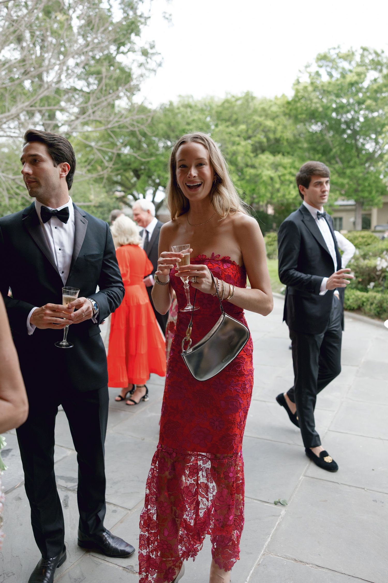Wedding guests in formal attire enjoying cocktails during an outdoor garden reception.