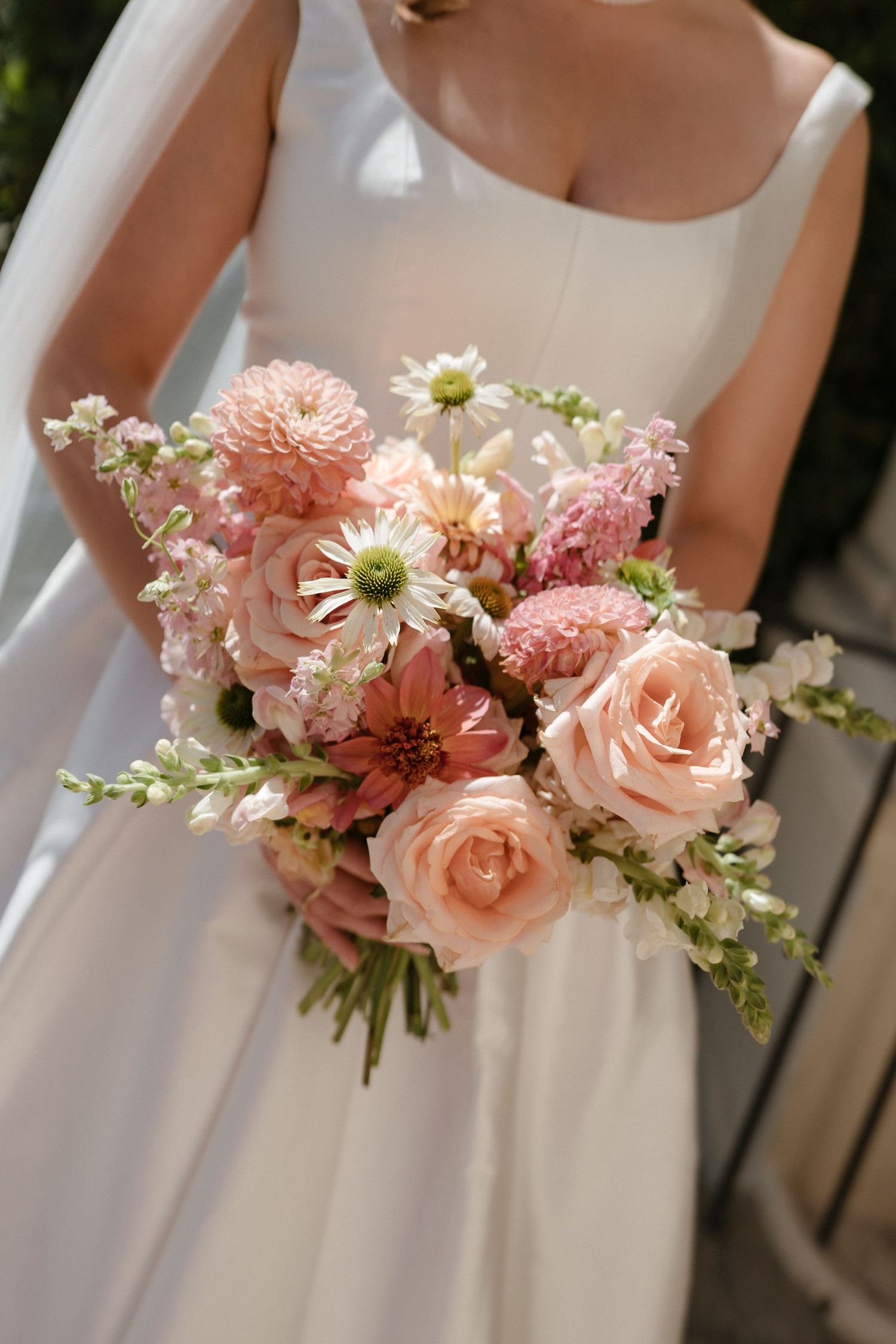 Delicate pink and white floral bouquet features roses, daisies and stock flowers against a white wedding dress background.