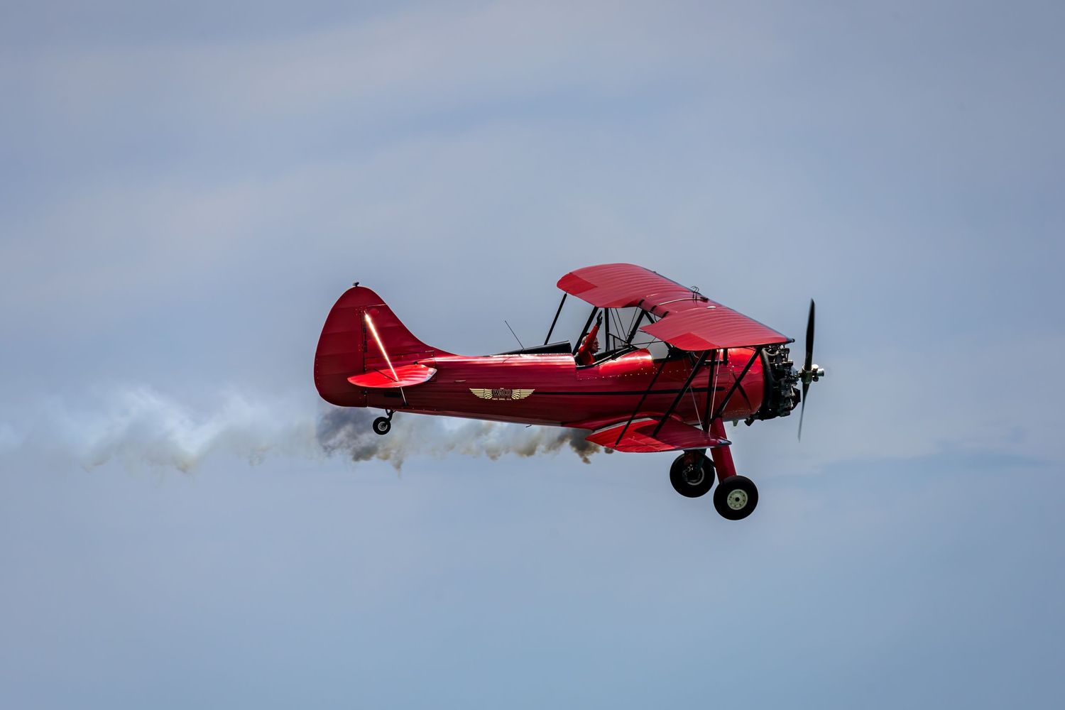 A red vintage aircraft flies across a cloudy blue sky on a bright day at Cocoa Beach Air Show 2025