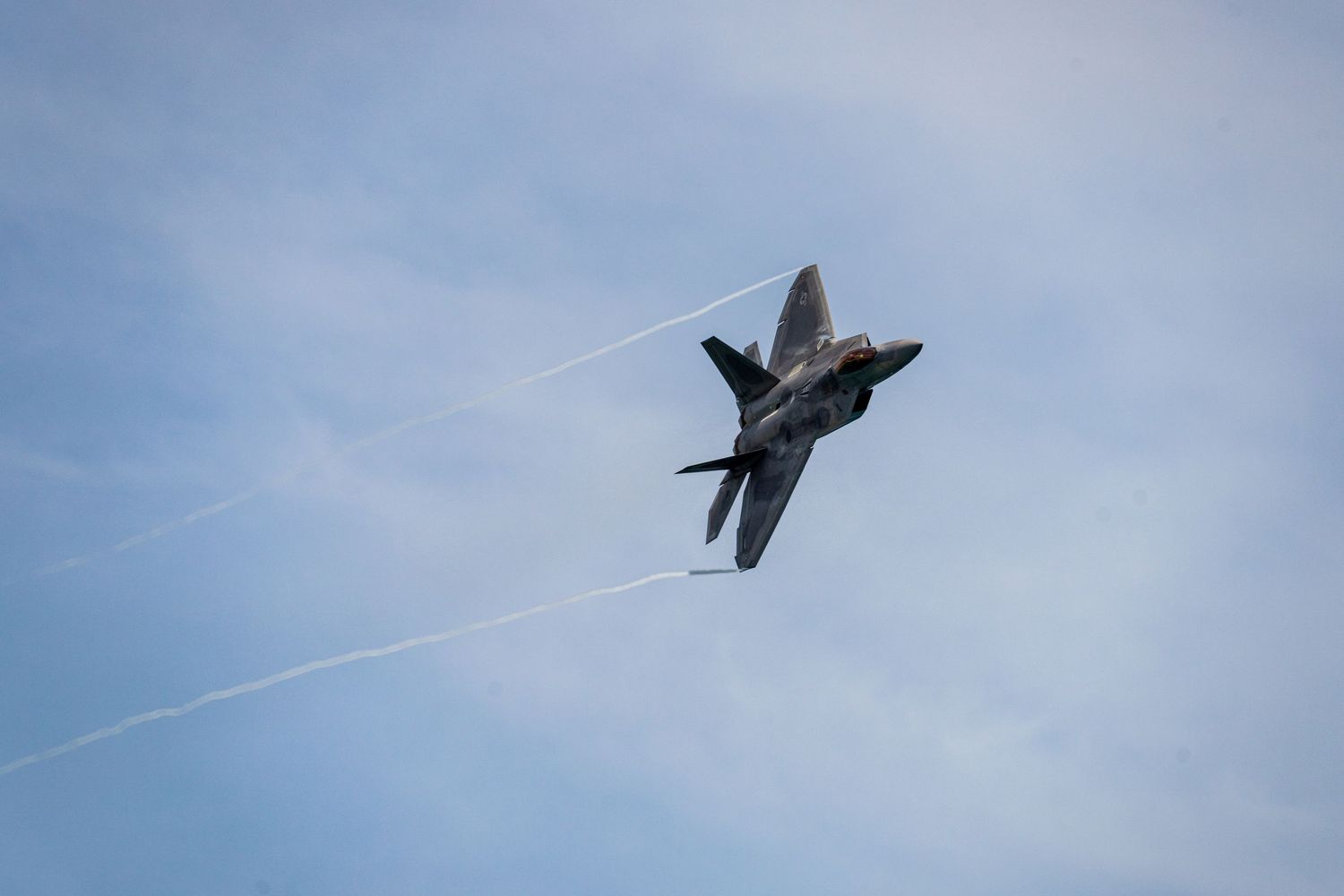 A series of photographs showing a fighter jet performing an arial maneuvers creating a vapor cone in blue sky at Cocoa Beach Air Show 2025