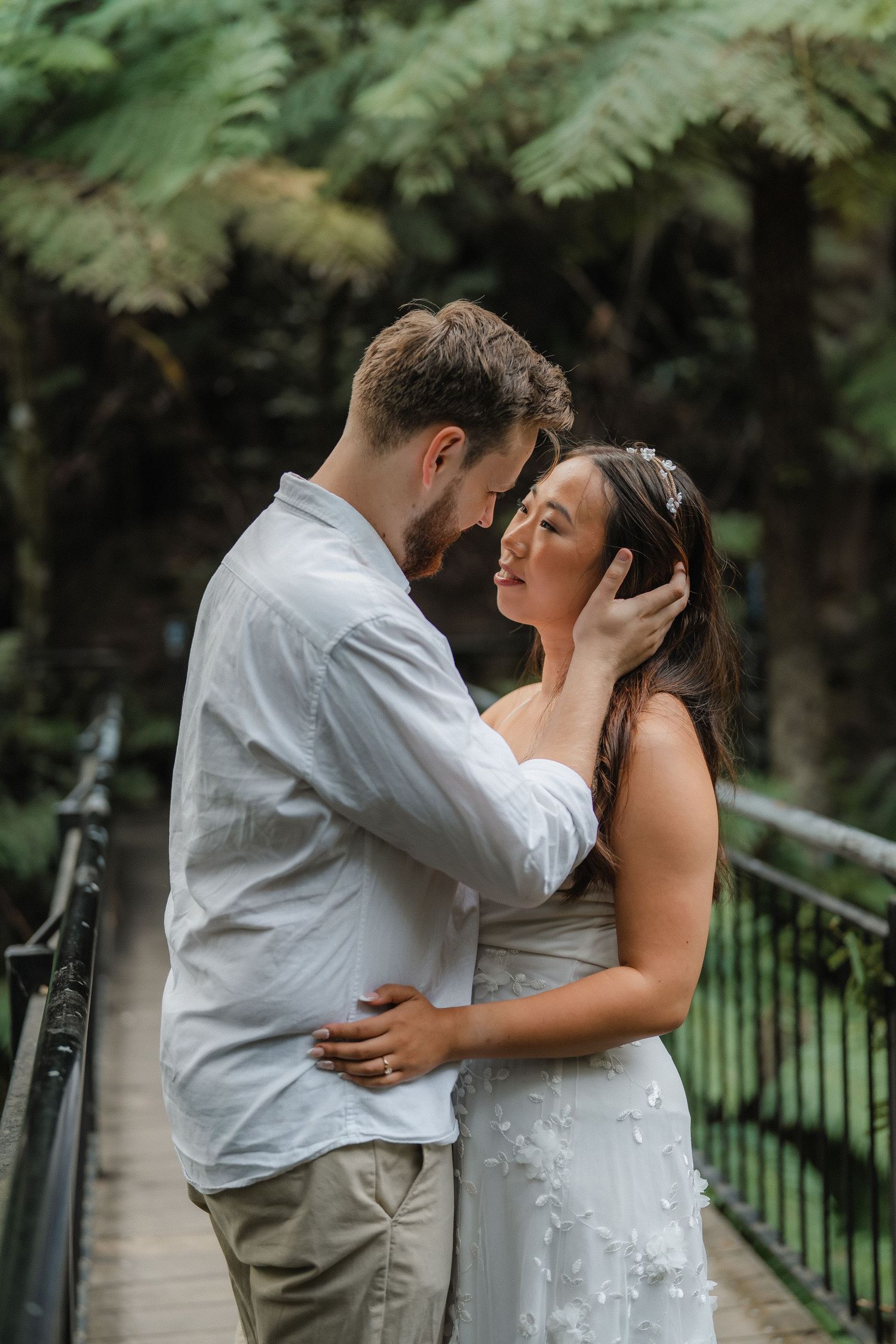Intimate moment between couple on wooden walkway with green ferns creating natural backdrop.