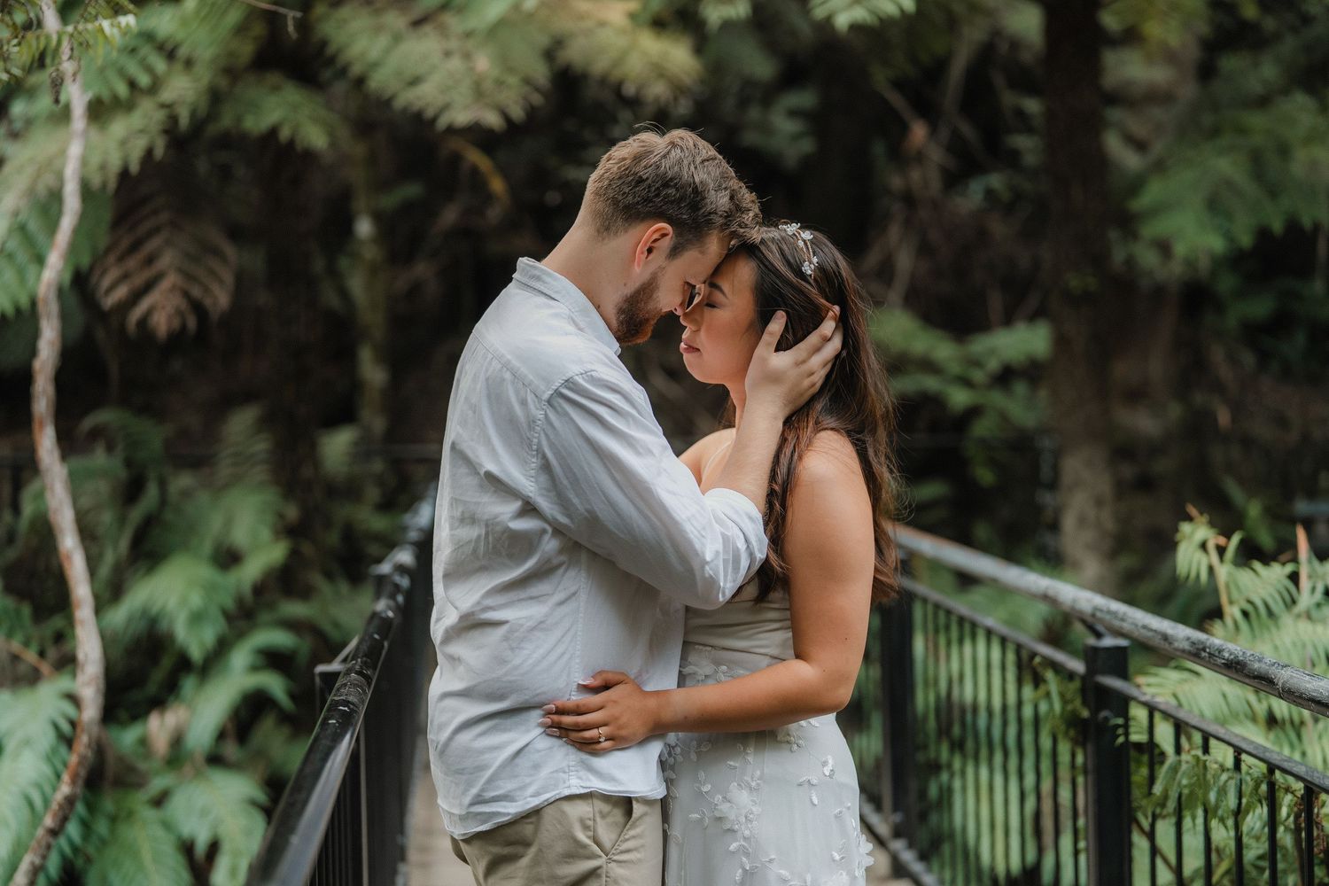 A romantic couple embraces in front of a lush forest waterfall during a photo session.