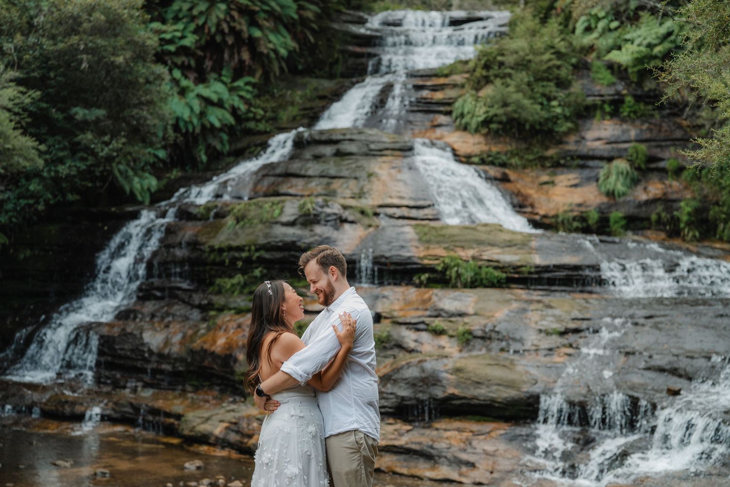 Scenic waterfall cascades down rocky ledges during a couple's intimate photoshoot.