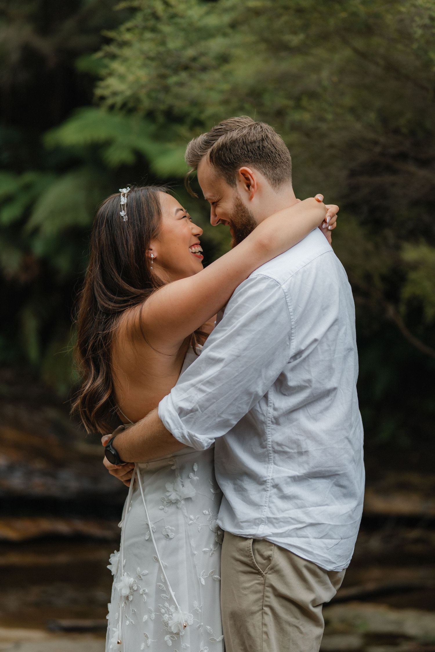 A candid moment of joy and laughter shared between a couple in a forest setting.