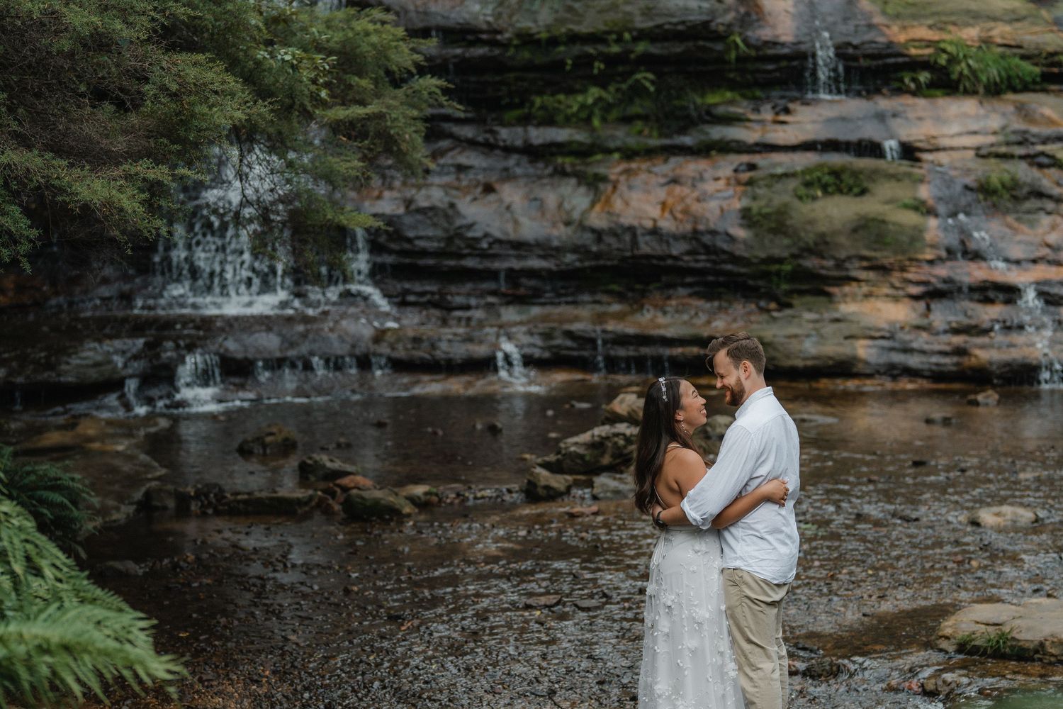 A couple shares an intimate moment by a rocky waterfall.