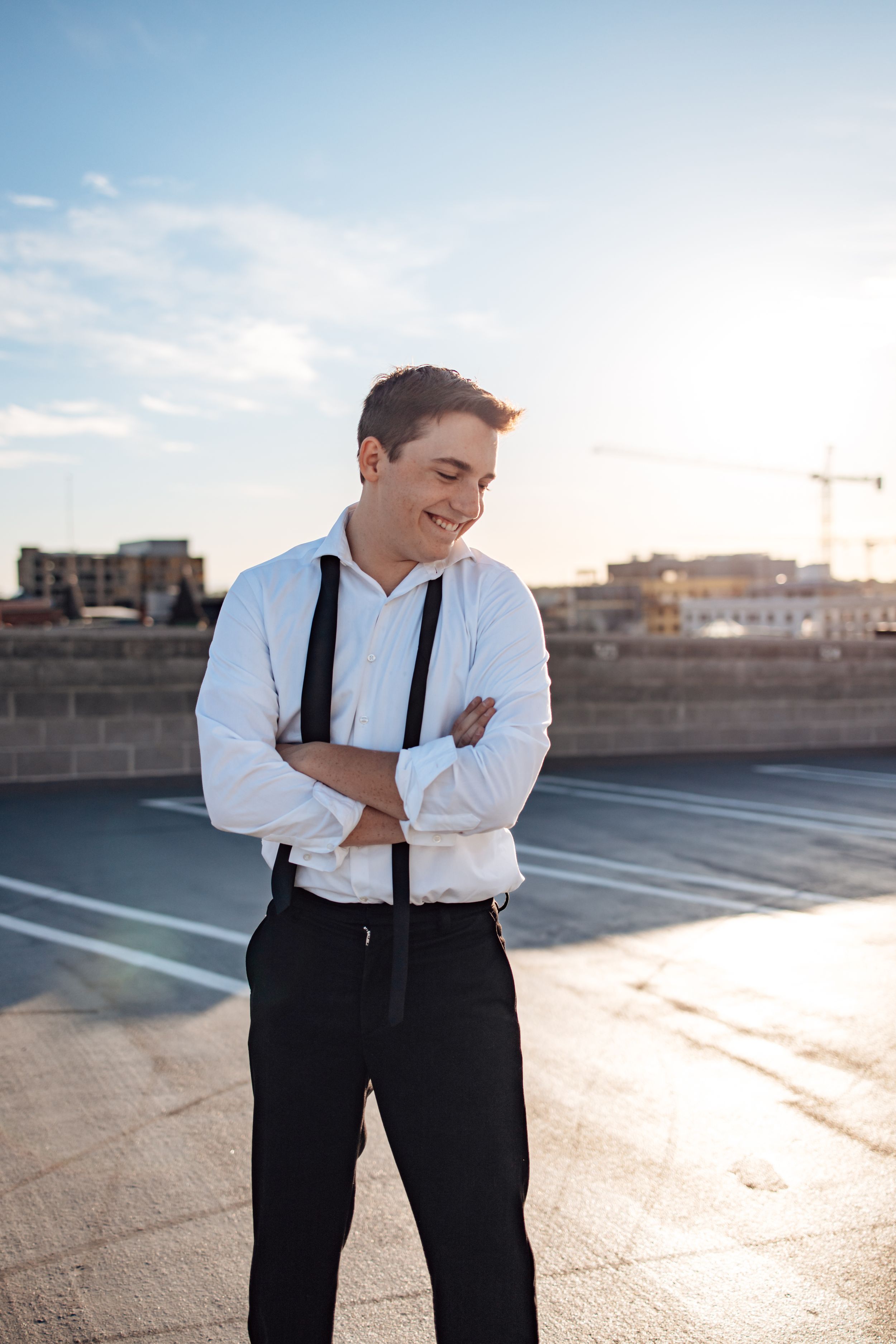 Person in formal attire laughs while standing on an urban rooftop at sunset.