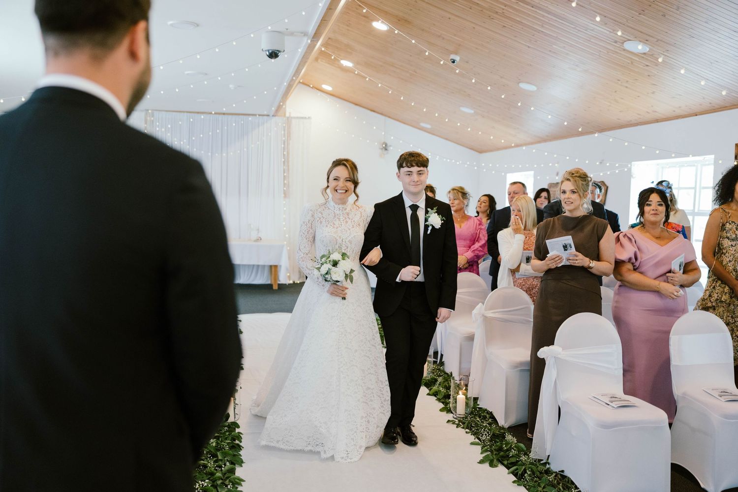 A couple walks down an aisle lined with guests while being showered with flower petals during a wedding ceremony.