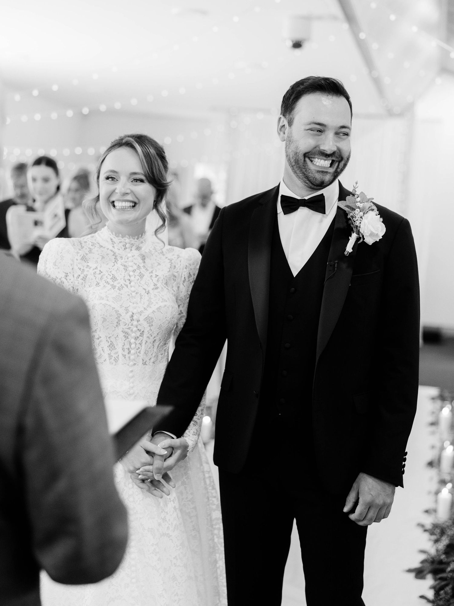 Black and white photo of a newlywed couple laughing during their wedding ceremony in an elegant indoor venue.