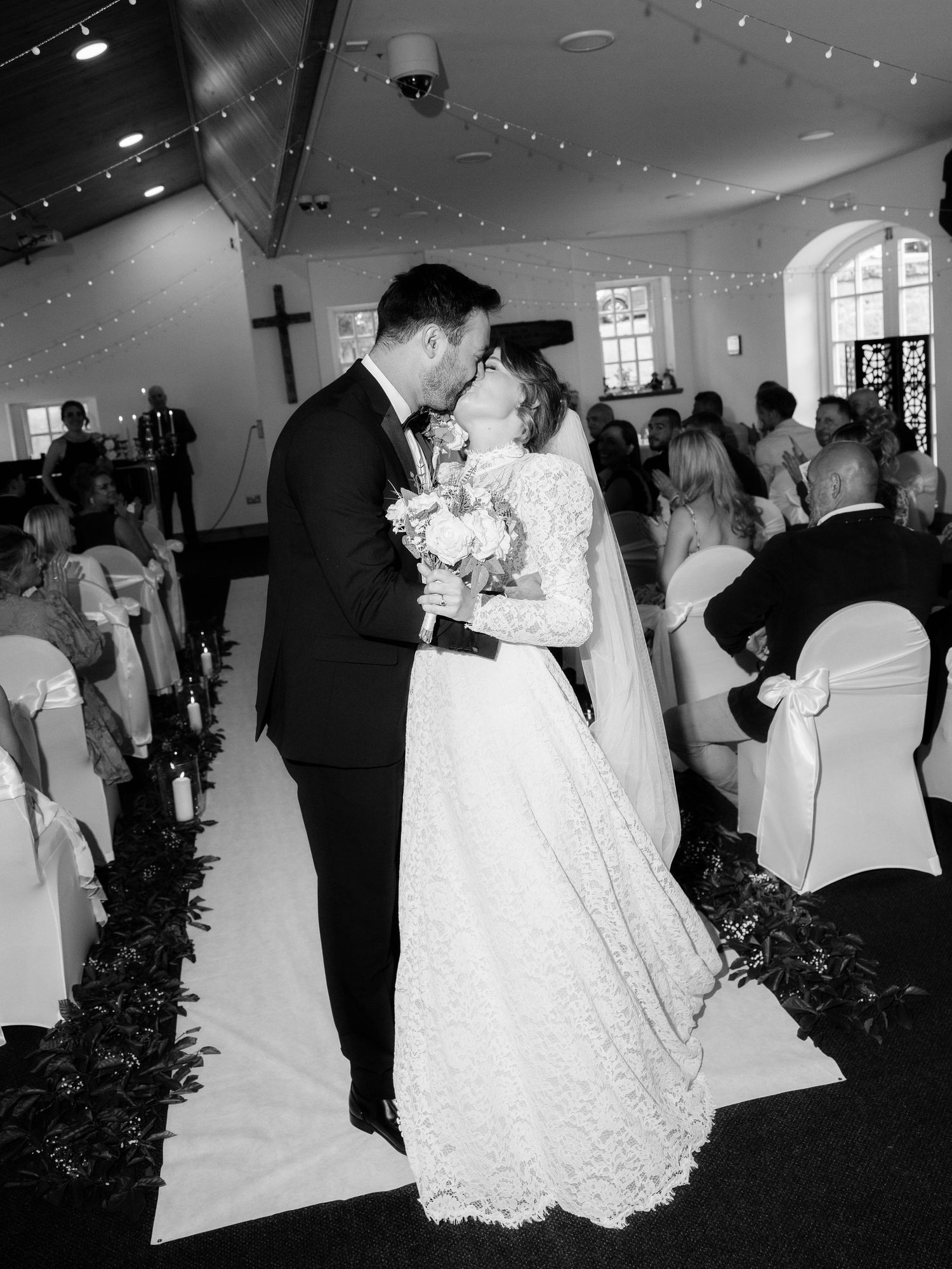 A church wedding ceremony showing the procession down the aisle with guests seated on either side in white chairs.