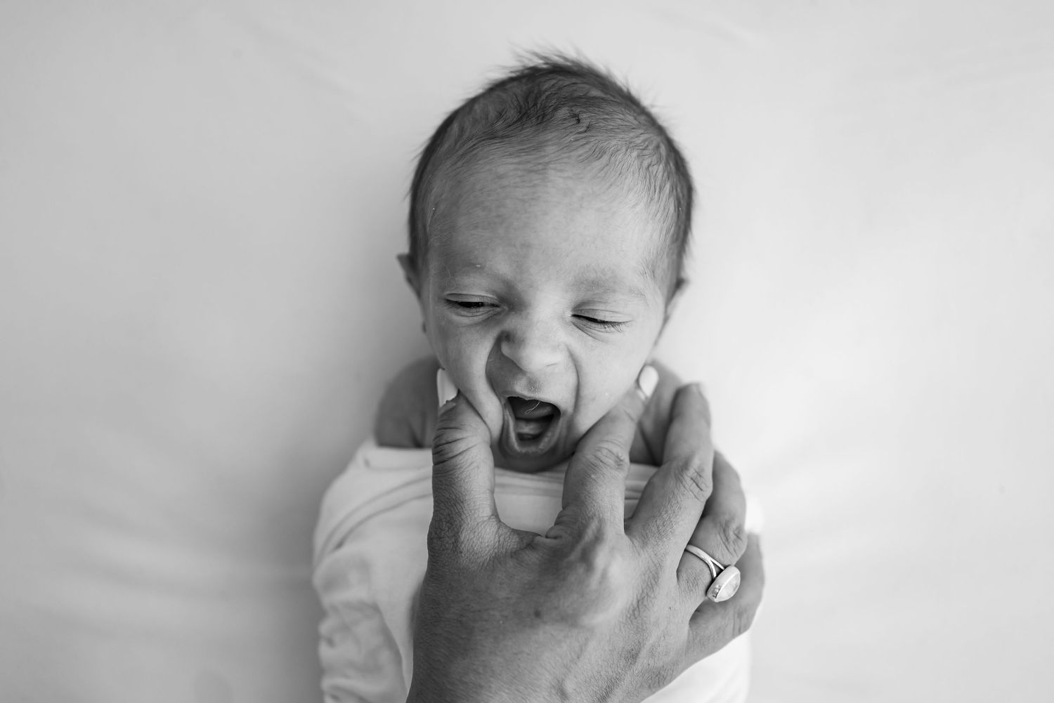 Black and white photo of a yawning newborn baby being held by an adult hand.