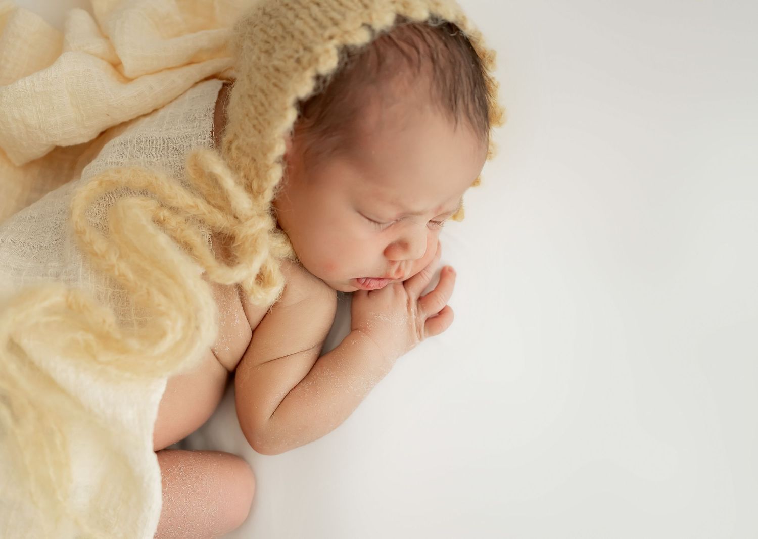 Adorable sleeping newborn baby wearing warm knit clothing and accessories in soft neutral tones.
