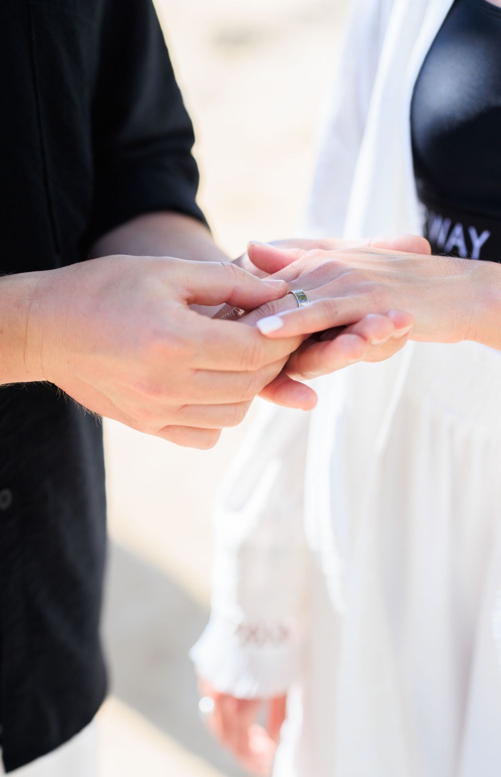 A groom placing a wedding ring on his bride's finger during an outdoor ceremony.