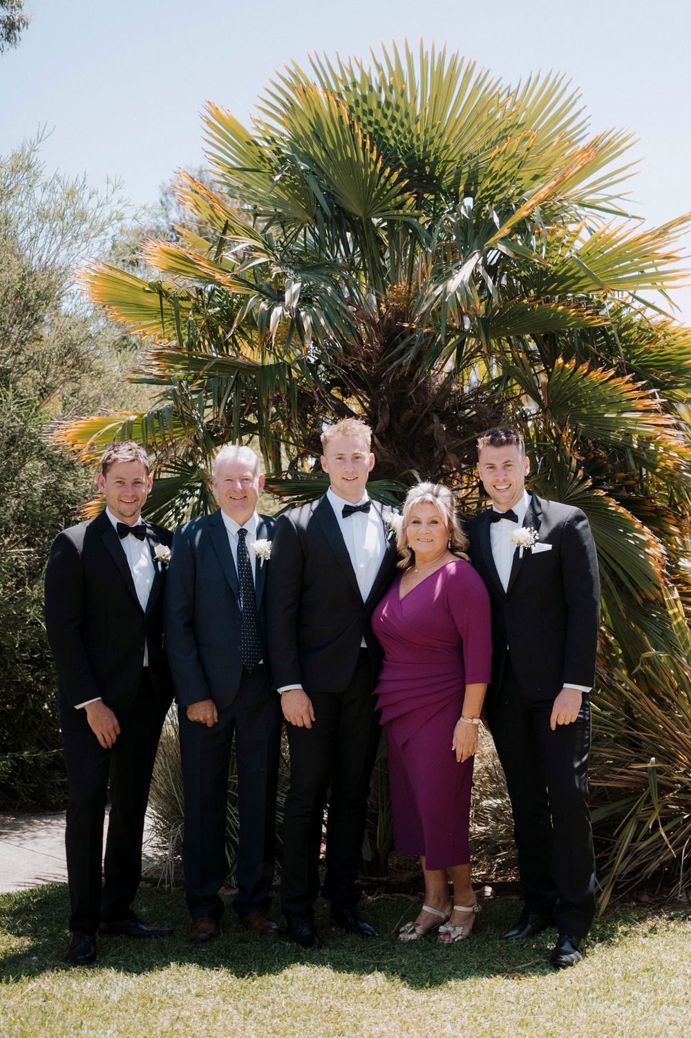 Wedding party poses together in front of a tropical palm tree on sunny day.